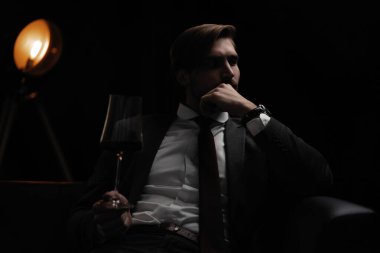 İş adamı dinleniyor. Karanlık bir odada bir bardak şarapla yakışıklı ve zarif bir adamın portresi.