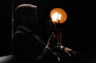 İş adamı dinleniyor. Karanlık bir odada bir bardak şarapla yakışıklı ve zarif bir adamın portresi.