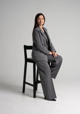 Beyaz arka planda bir sandalyede oturan neşeli genç bir iş kadınının portresi. Tüm vücut