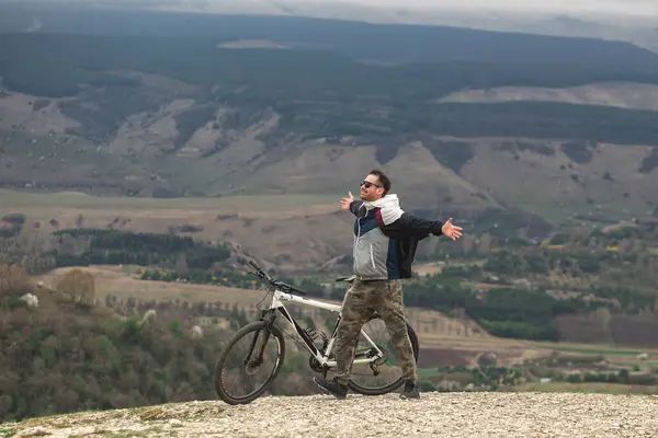 A happy man climbed the mountain on a bicycle and rejoices in the victory