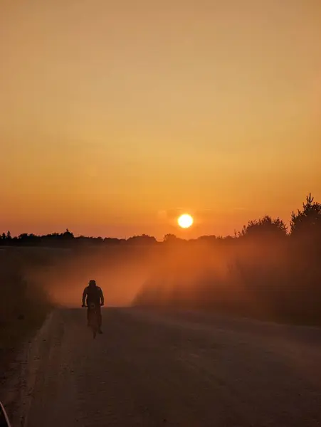 Silhouette of a cyclist on a mountain bike riding a trail in a field on a dramatic sunset background. High quality photo