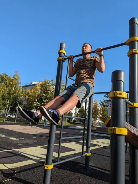 Normal man exercising outside. Holding his upper body above horizontal bar. Real people.