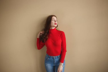 Sade pastel bej arka plan stüdyosunda izole edilmiş kırmızı balıkçı yakalı 20 'li yaşlarda çekici bir kadın. Halk yaşam tarzı konsepti