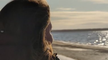 Güzel bir genç kadın güneşli bir günde kış nehrinin arka planında güneş gözlüğü takar. Yüksek kalite 4K görüntü. Yüksek kalite 4k görüntü