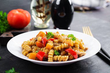 Sebze makarna fusilli corti bucati ile patlıcan, tatlı biber ve siyah masada beyaz tabakta tavuk..