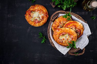 Çocuklar için mini pizza, jambonlu küçük açık turtalar, domates sosu, mozzarella ve peynir sepetinde koyu bir arka planda. Üst görünüm