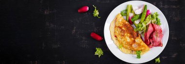 Kahvaltıda. Peynirli omlet ve taze salata, salam. Frittata - İtalyan omleti. Ketogenik öğle yemeği. Üst görünüm, afiş