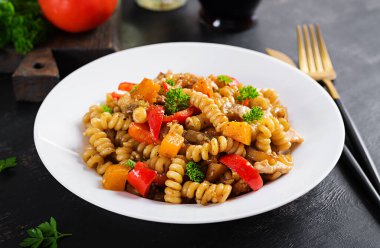 Sebze makarna fusilli corti bucati ile patlıcan, tatlı biber ve siyah masada beyaz tabakta tavuk..