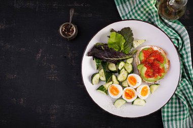 Breakfast. Healthy open sandwich on  toast with avocado and red caviar, boiled eggs, cucumber salad on white plate. Healthy protein food. Top view