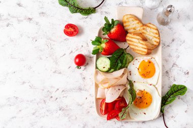 Fried eggs with ham, tomatoes, cucumber, strawberries and toasts. Delicious English Breakfast. Brunch. Top view, overhead