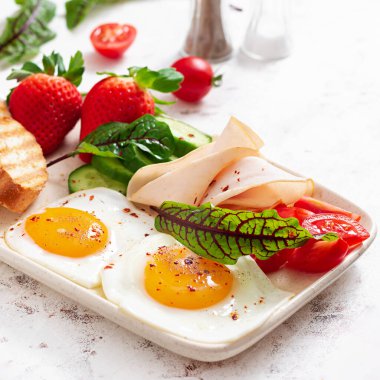 Fried eggs with ham, tomatoes, cucumber, strawberries and toasts. Delicious English Breakfast. Brunch.