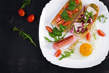 Breakfast. Fried egg, sausage and sandwiches with pesto, cheese, tomatoes with green. Top view, above