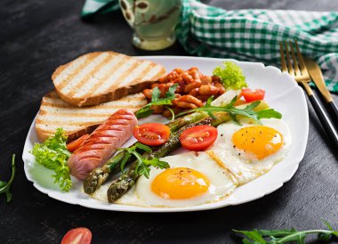 Keto breakfast. Breakfast. Fried eggs, bread toast, green asparagus, beans and sausage on white plate.