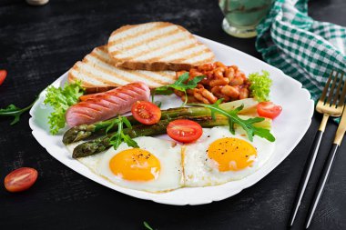 Keto breakfast. Breakfast. Fried eggs, bread toast, green asparagus, beans and sausage on white plate.