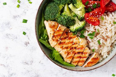 Delicious buddha bowl with grilled chicken, fresh vegetables and rice on a light background. Top view, above