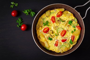 Omelette with tomatoes,  zucchini and potatoes on dark background. Healthy diet food for breakfast. Tasty morning food. Top view, flat lay.