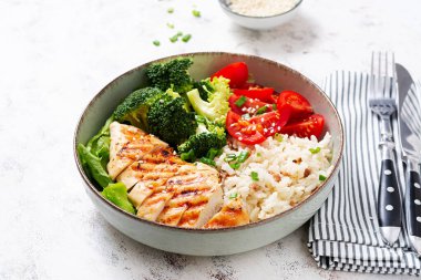 Delicious buddha bowl with grilled chicken, fresh vegetables and rice on a light background.