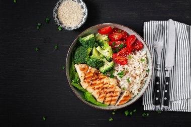 Delicious buddha bowl with grilled chicken, fresh vegetables and rice on a dark background. Top view, above