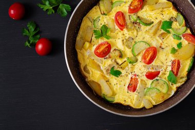 Omelette with tomatoes,  zucchini and potatoes on dark background. Healthy diet food for breakfast. Tasty morning food. Top view, flat lay.