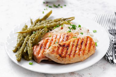 Chicken fillet cooked on a grill and garnish of rice, green beans.