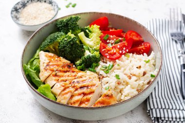 Delicious buddha bowl with grilled chicken, fresh vegetables and rice on a light background.
