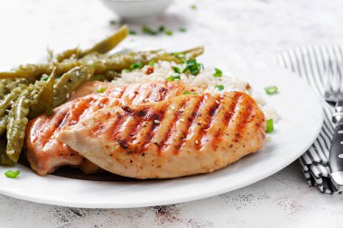 Chicken fillet cooked on a grill and garnish of rice, green beans.