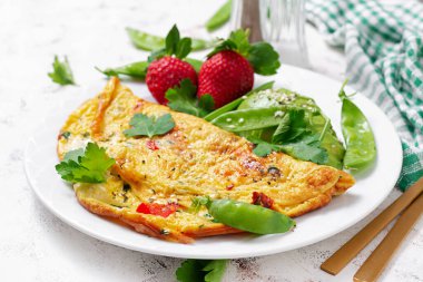 Omelette with tomatoes, feta cheese and avocado on white plate.