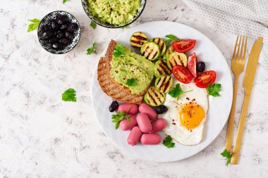 Fried egg with mini sausage, tomatoes, grilled zucchini, black olives and toasts with guacamole. English Breakfast. Brunch. Top view
