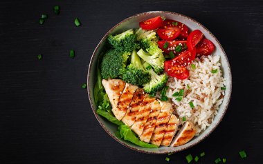 Delicious buddha bowl with grilled chicken, fresh vegetables and rice on a dark background. Top view, above