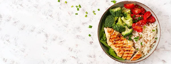 Delicious buddha bowl with grilled chicken, fresh vegetables and rice on a light background. Top view, banner