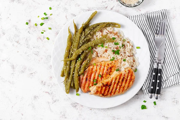 Chicken fillet cooked on a grill and garnish of rice, green beans. Top view