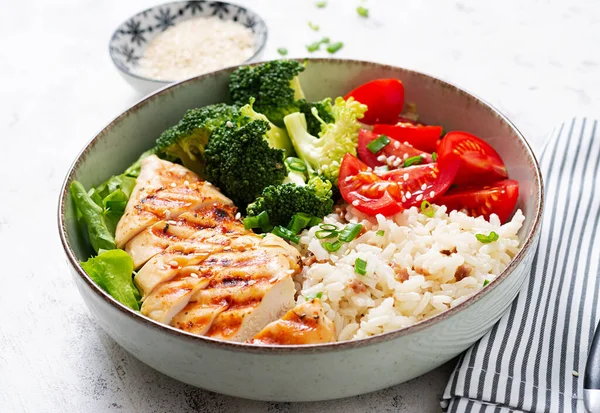 Delicious buddha bowl with grilled chicken, fresh vegetables and rice on a light background.