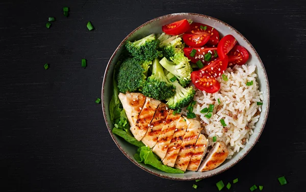 Delicious buddha bowl with grilled chicken, fresh vegetables and rice on a dark background. Top view, above