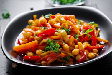 Vegetable stew of chickpeas, carrot, sweet peppers, onions, garlic and tomato sauce with lemon on the dark table. Oriental cuisine.