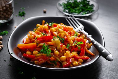 Vegetable stew of chickpeas, carrot, sweet peppers, onions, garlic and tomato sauce with lemon on the dark table. Oriental cuisine.