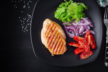 Grilled chicken breast. Fried chicken fillet and fresh vegetable salad of tomatoes, red onions and lettuce. Chicken meat with salad. Keto diet. Top view, flat lay