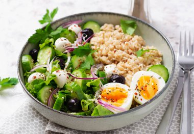 Breakfast oatmeal porridge with boiled eggs, cucumber, mozzarella cheese and green herbs. Healthy balanced food.