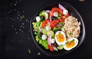 Healthy breakfast. Greek inspired savory oatmeal with fresh cucumber, tomatoes, olives, lettuce, mozzarella cheese and boiled egg. Top view