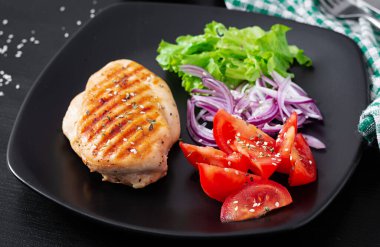 Grilled chicken breast. Fried chicken fillet and fresh vegetable salad of tomatoes, red onions and lettuce. Chicken meat with salad.
