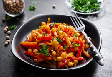 Vegetable stew of chickpeas, carrot, sweet peppers, onions, garlic and tomato sauce with lemon on the dark table. Oriental cuisine.