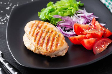 Grilled chicken breast. Fried chicken fillet and fresh vegetable salad of tomatoes, red onions and lettuce. Chicken meat with salad.