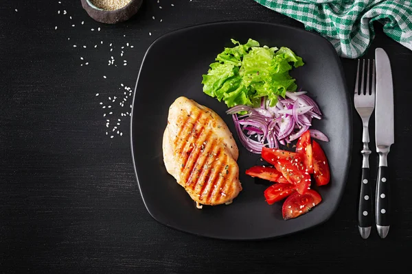 Grilled chicken breast. Fried chicken fillet and fresh vegetable salad of tomatoes, red onions and lettuce. Chicken meat with salad. Keto diet. Top view, flat lay