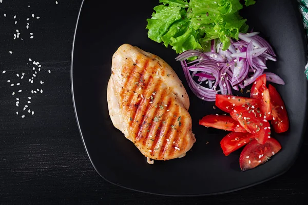Grilled chicken breast. Fried chicken fillet and fresh vegetable salad of tomatoes, red onions and lettuce. Chicken meat with salad. Keto diet. Top view, flat lay