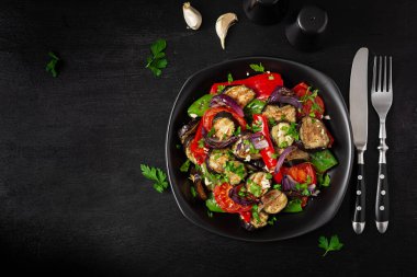 Grilled vegetables eggplant, bell pepper, zucchini, red onion, tomato with garlic on a black plate. Top view, above