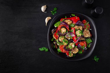 Grilled vegetables eggplant, bell pepper, zucchini, red onion, tomato with garlic on a black plate. Top view, above