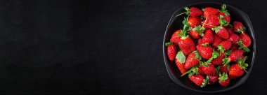 Strawberries in a black plate on dark background. Top view, banner