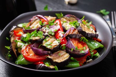 Grilled vegetables eggplant, bell pepper, zucchini, red onion, tomato with garlic on a black plate.