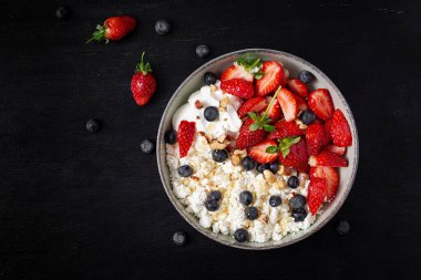Cottage cheese, curd cheese with fresh strawberries, blueberries, nuts and yogurt in a bowl.  Healthy dairy product rich in calcium and protein. Top view, above