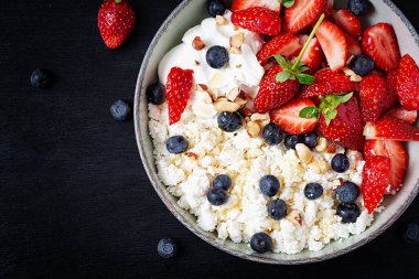 Cottage cheese, curd cheese with fresh strawberries, blueberries, nuts and yogurt in a bowl.  Healthy dairy product rich in calcium and protein. Top view, above