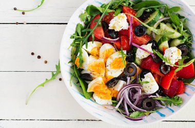 Kahvaltıda. Yunan salatası ve haşlanmış yumurta. Domates, salatalık, zeytin, roka ve krem peynirli taze sebze salatası. Moda yemekler. Üst manzara, düz uzanma